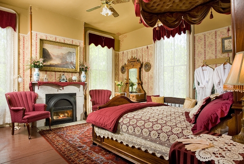 A luxurious bedroom with a four-poster bed, a cozy fireplace, plush armchairs, and a window with she