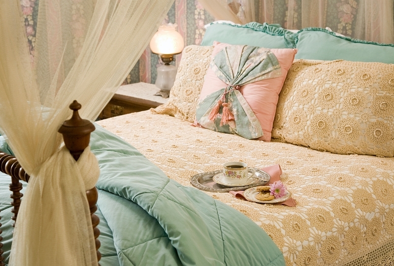 A cozy bed with a white canopy, decorative pillows, and a tray with a cup and saucer, perfect for a