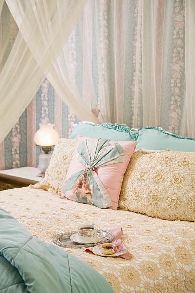 A cozy bed with a white canopy, decorative pillows, a bedside lamp, and a tray with a cup and saucer