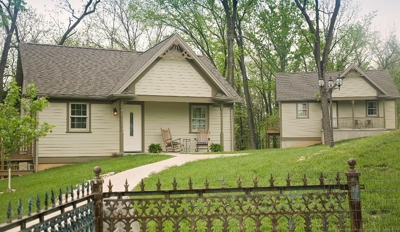 Two charming cottages with inviting front porches, set on a tree-lined property with a decorative fe