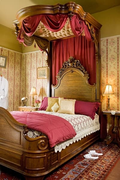 A romantic bedroom with a large four-poster bed with a canopy, a bedside table with a lamp, and a ru