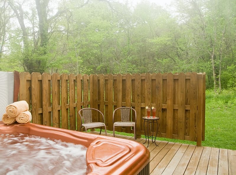 A private hot tub oasis with a wooden fence and comfortable seating, perfect for relaxation in a pea