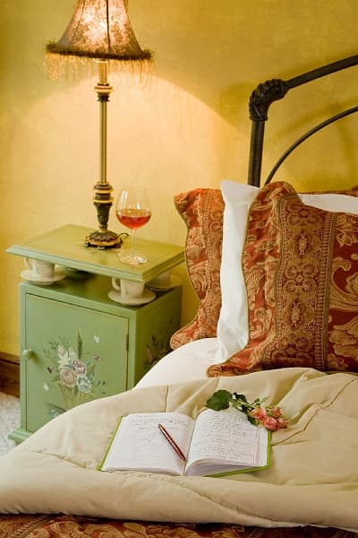 A romantic bedside scene with a lamp, a glass of wine, a journal, and a rose, inviting relaxation an