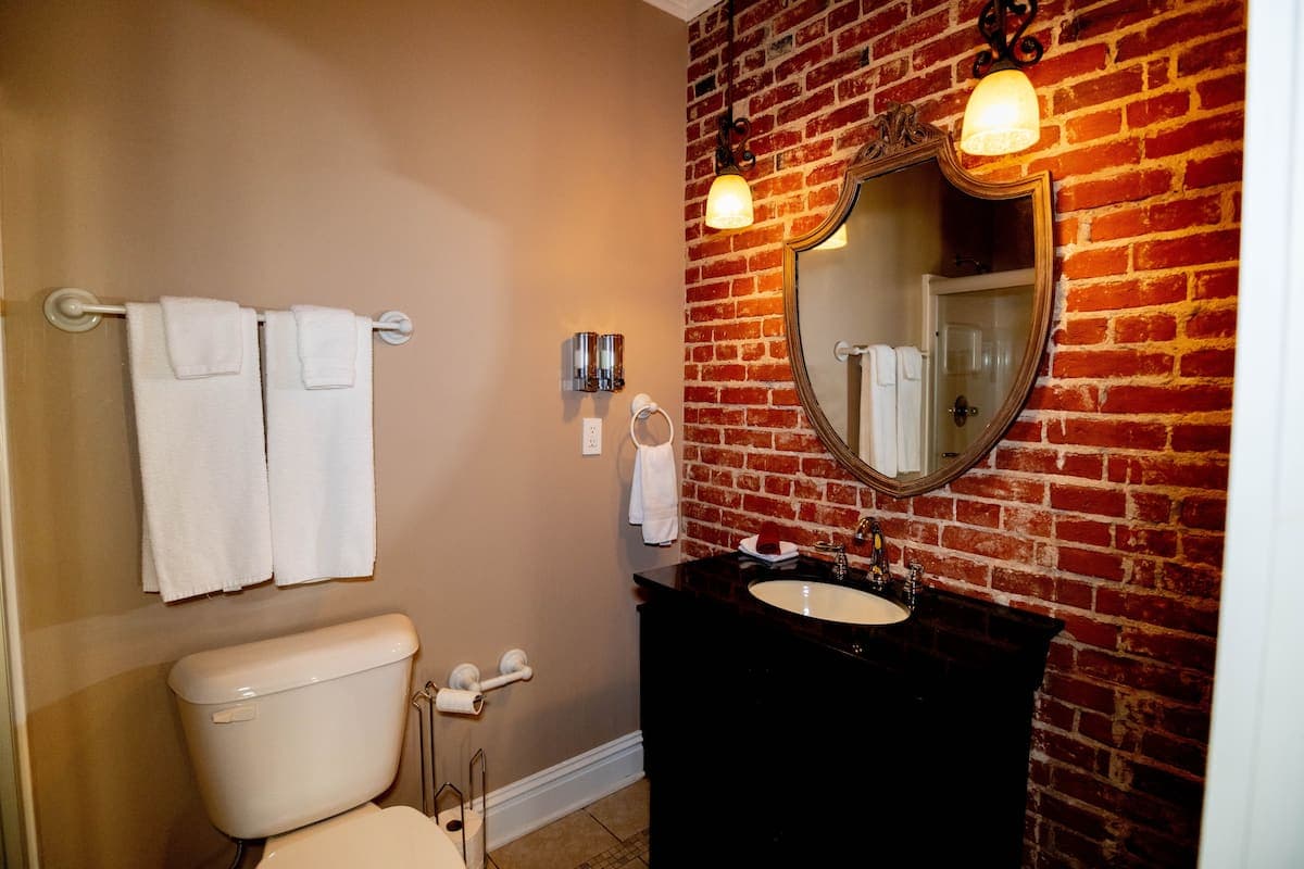 A stylish bathroom with an exposed brick accent wall, a dark vanity with a white sink, an ornate mi