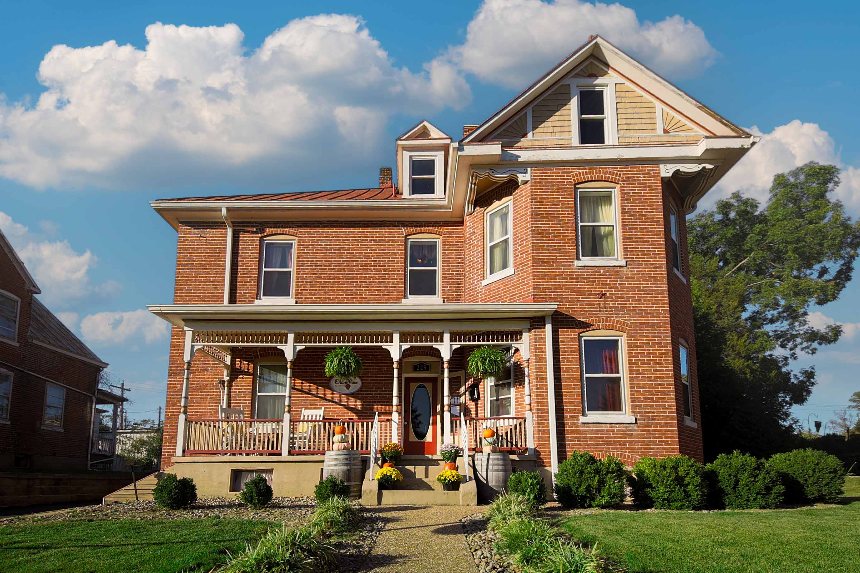 A grand red brick house with a prominent front porch, ornate white columns, and multiple windows, s