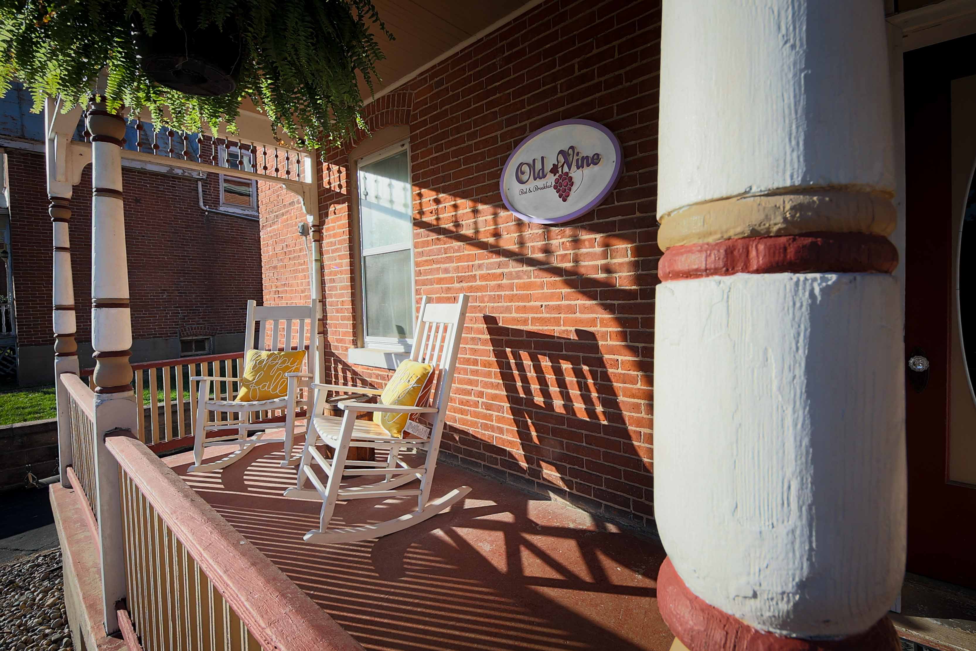 A inviting front porch with two white rocking chairs featuring yellow pillows, an "Old Vine" sign on