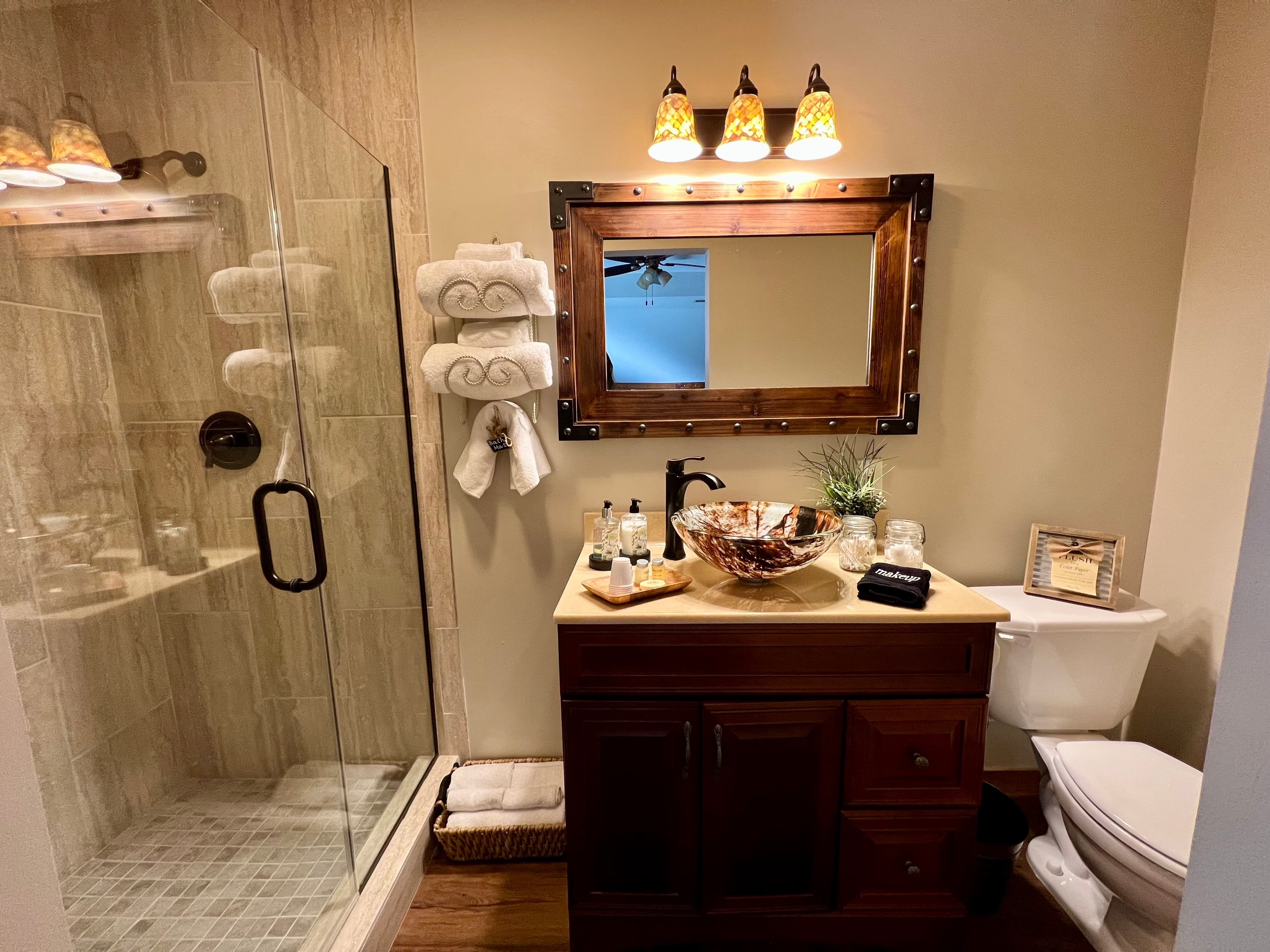 bathroom vanity with brown floating bowl, toilet, wooden framed rectangle mirror and three lights ab