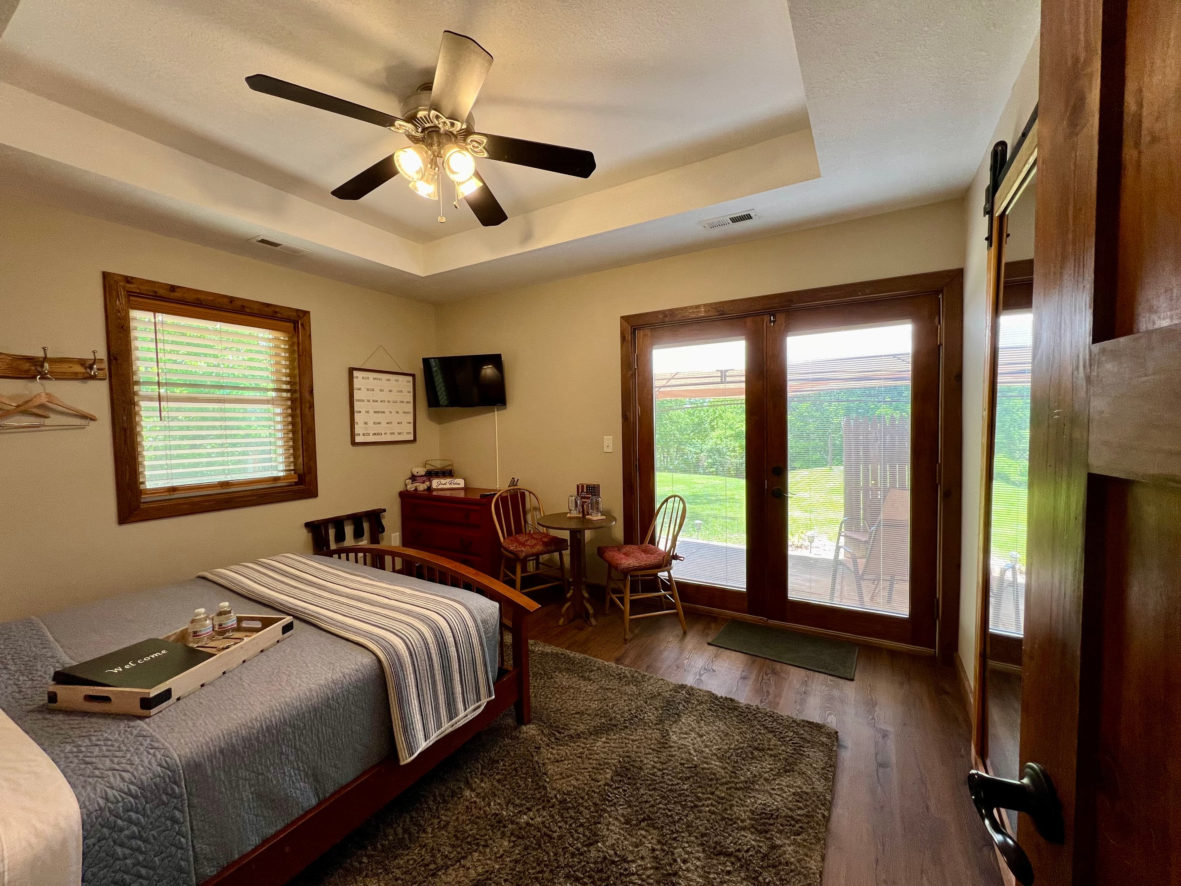 brown wooden bed with blue quilt and white and blue accent blanket, two wooden chairs with round bro