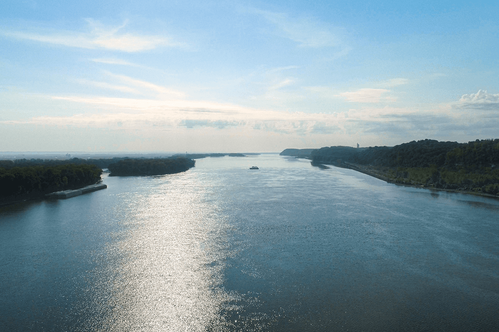 A serene river scene with reflective water leading to lush green hills under a blue sky.