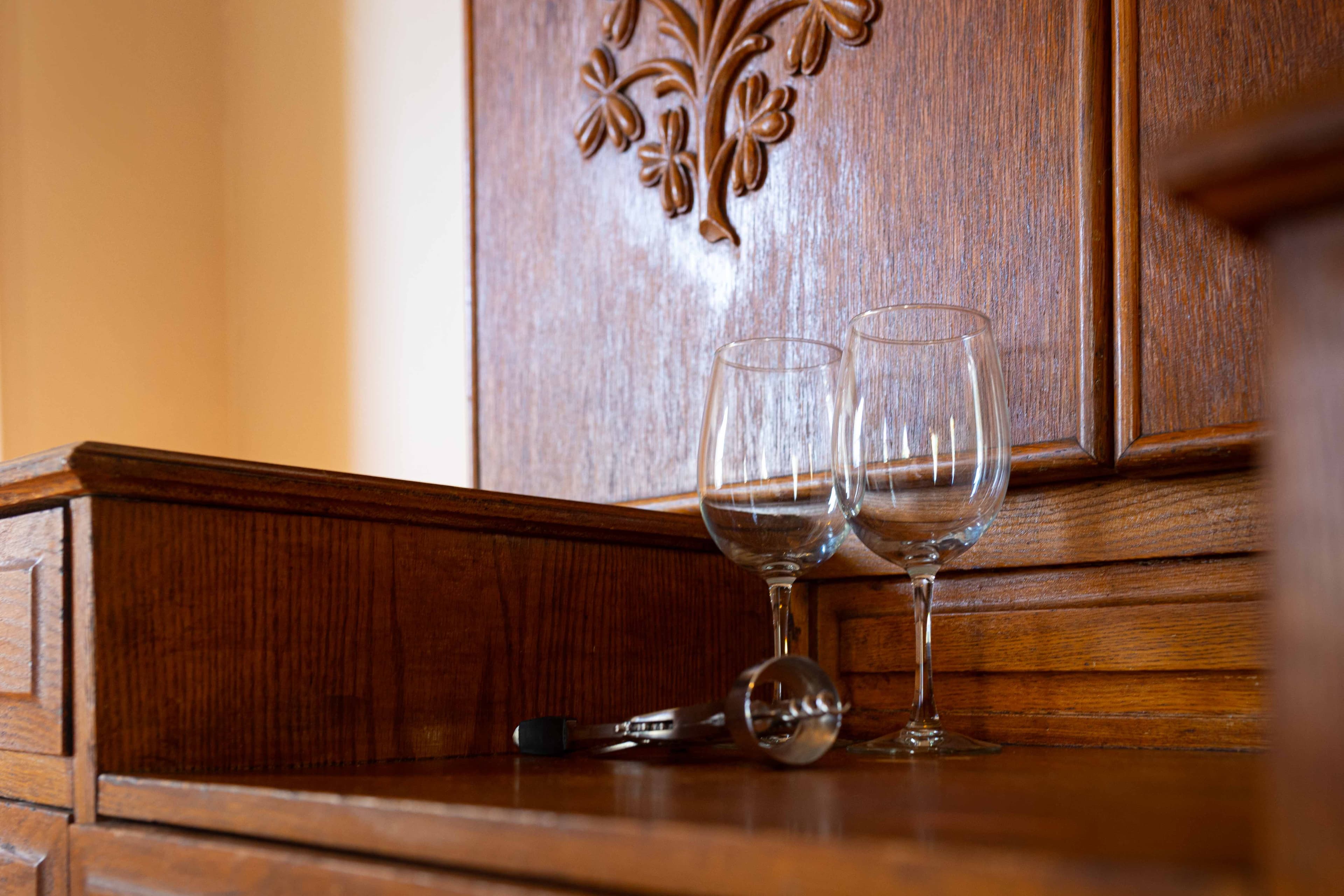 Two wine glasses and a corkscrew on a wooden countertop.