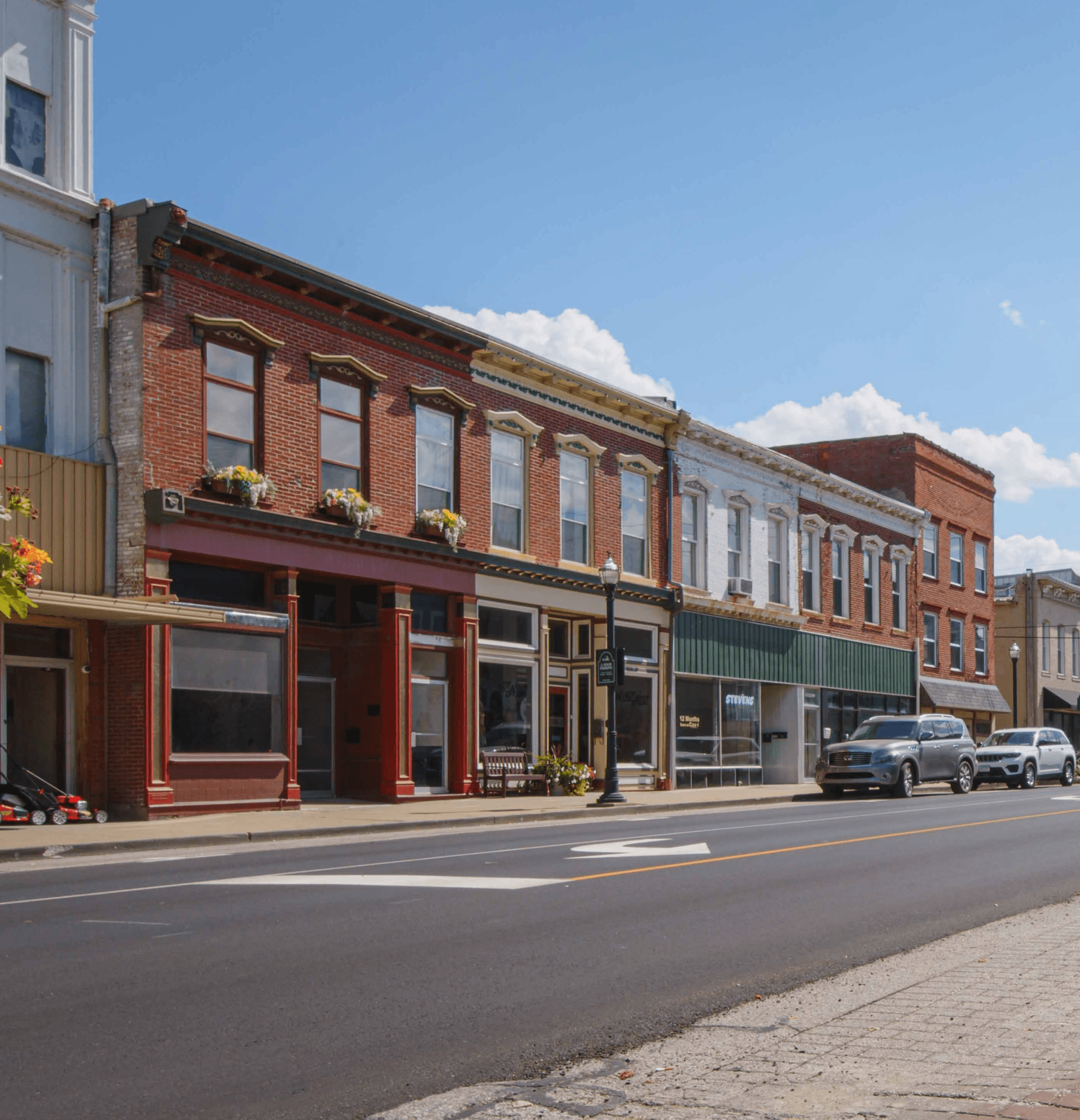A row of historic brick buildings lining a quiet street under a blue sky.
