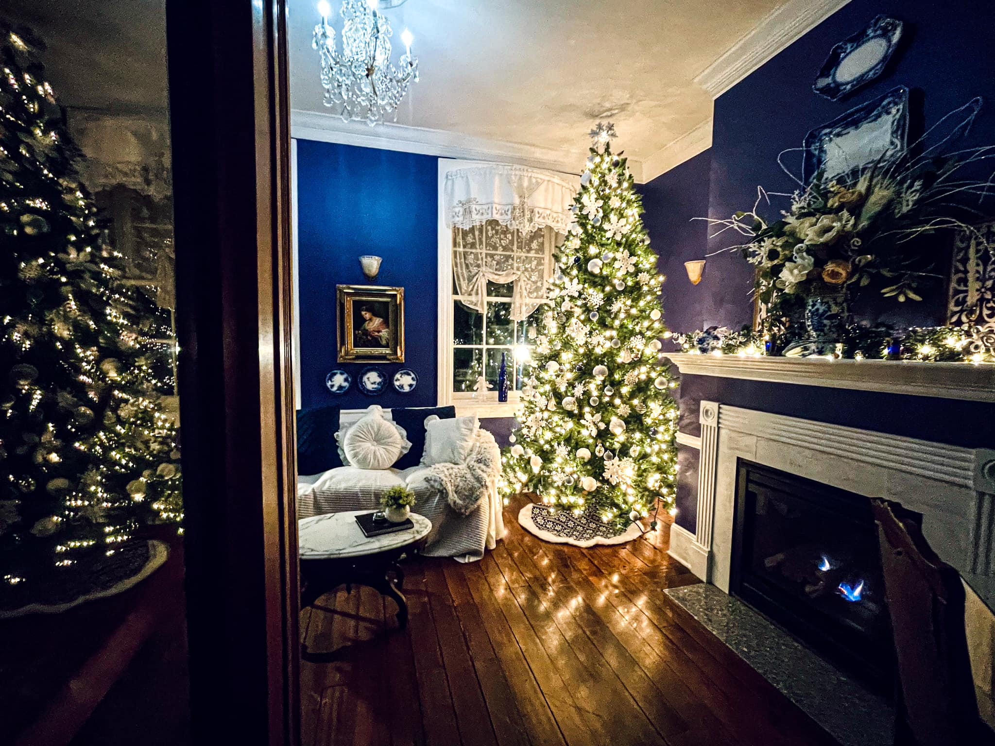 A cozy living room decorated for the holidays, featuring a brightly lit Christmas tree and a fireplace.