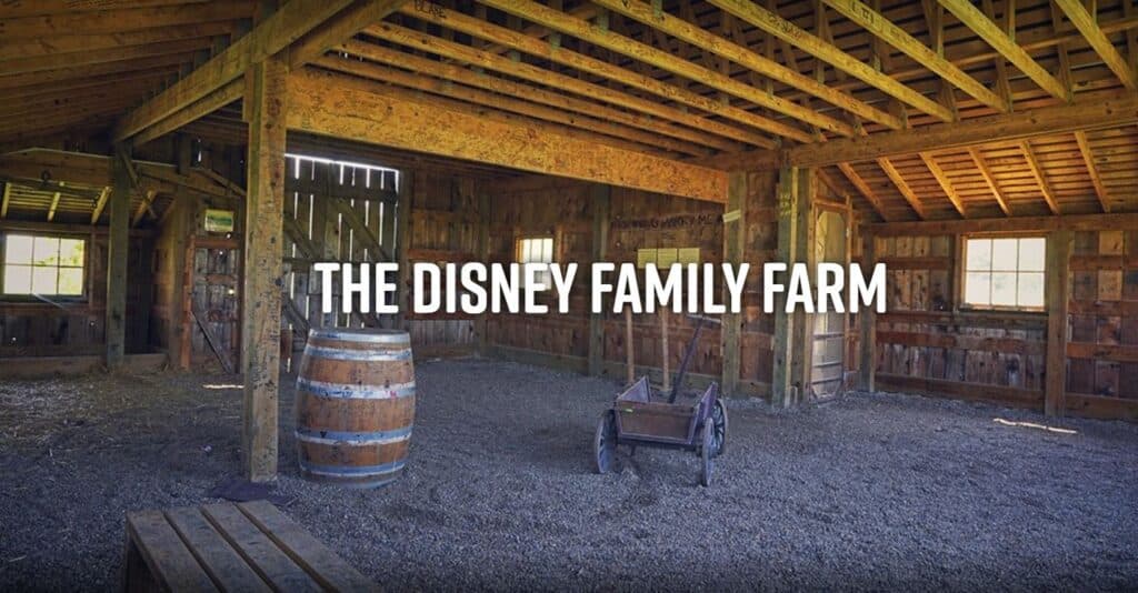 Interior of a rustic barn at the Disney Family Farm, featuring wooden walls, a barrel, and a cart.
