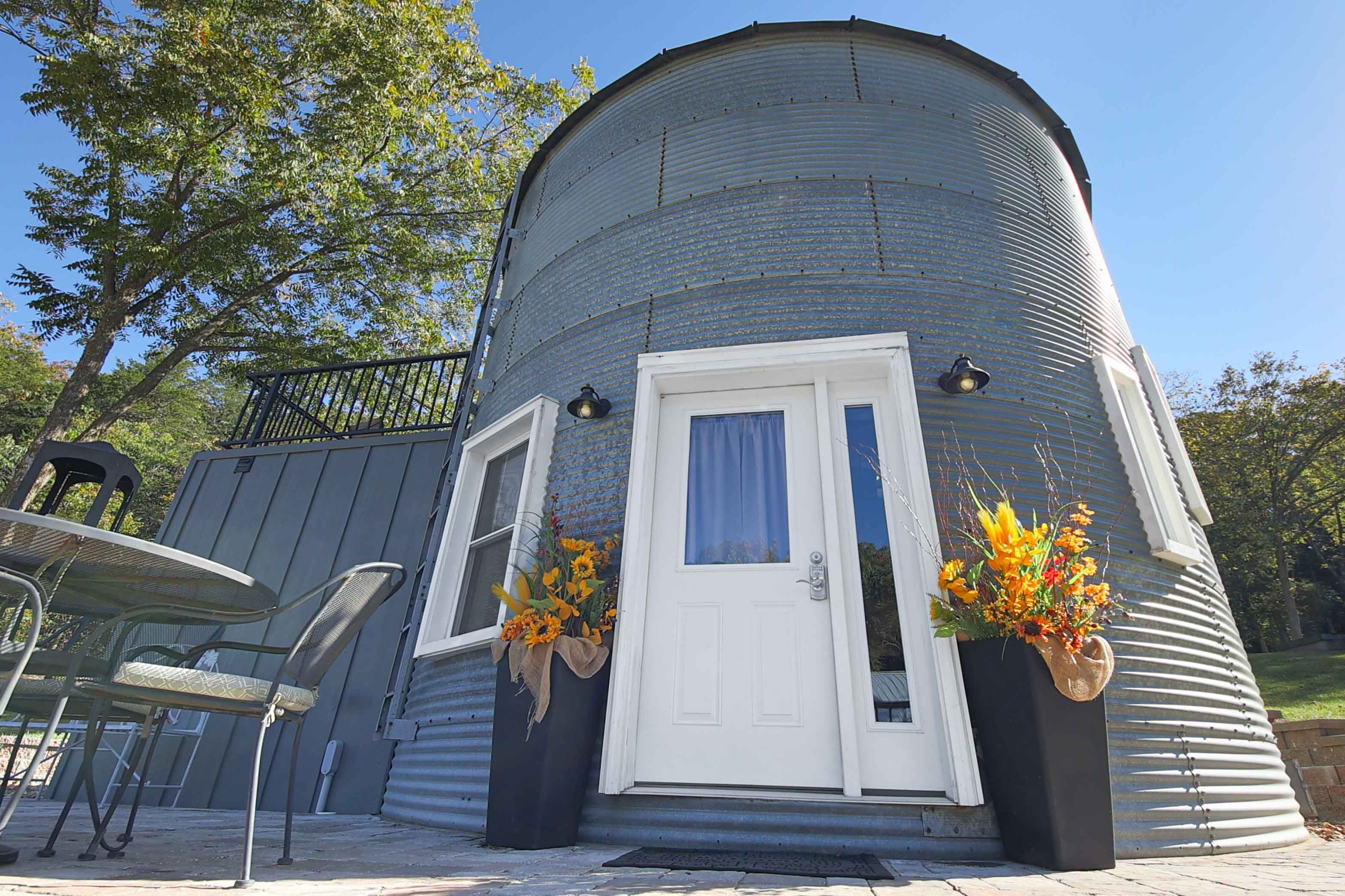 A round, metal building with a white door and vibrant flower arrangements by the entrance.