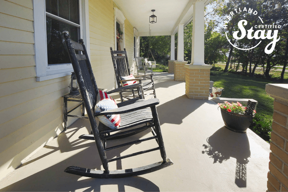 A cozy porch with two rocking chairs and a flower pot, featuring natural light and greenery.
