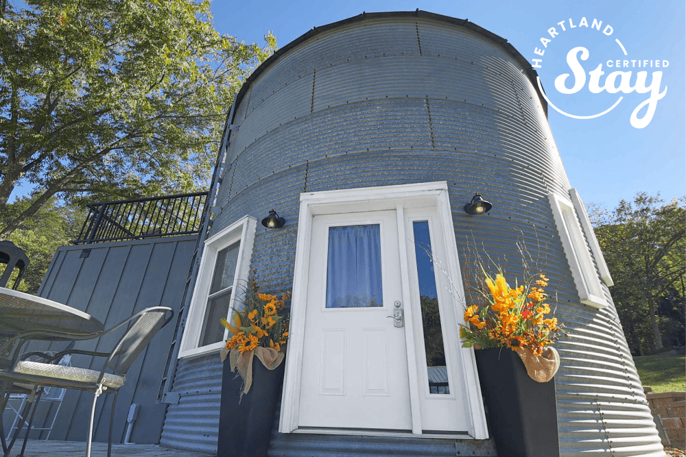 A cozy, round metal cabin entrance adorned with vibrant flower arrangements and a small outdoor seating area.