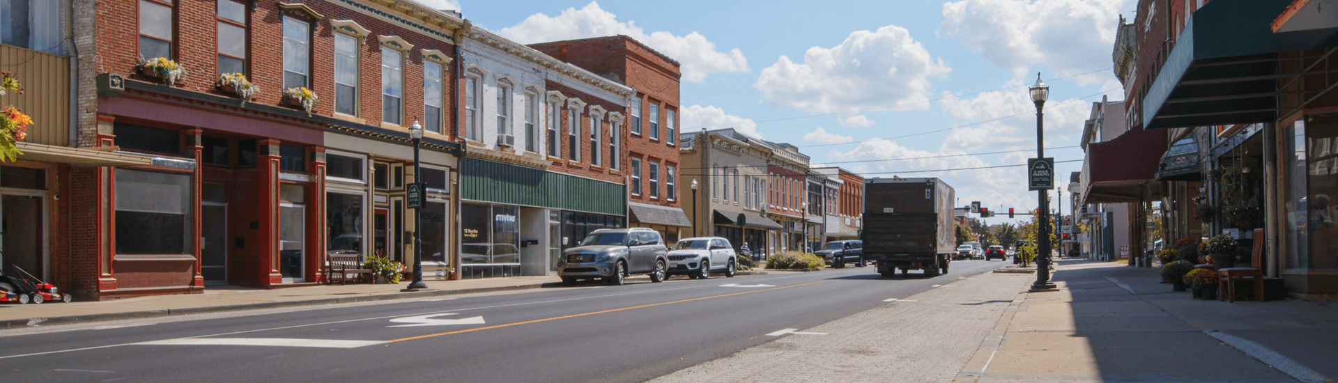 A charming downtown street with brick buildings, parked cars, and clear blue skies.