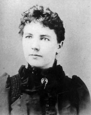 A black-and-white portrait of a woman with short, curly hair, wearing a Victorian-style dress. A black-and-white portrait of a woman with short, curly hair, wearing a Victorian-style dress.