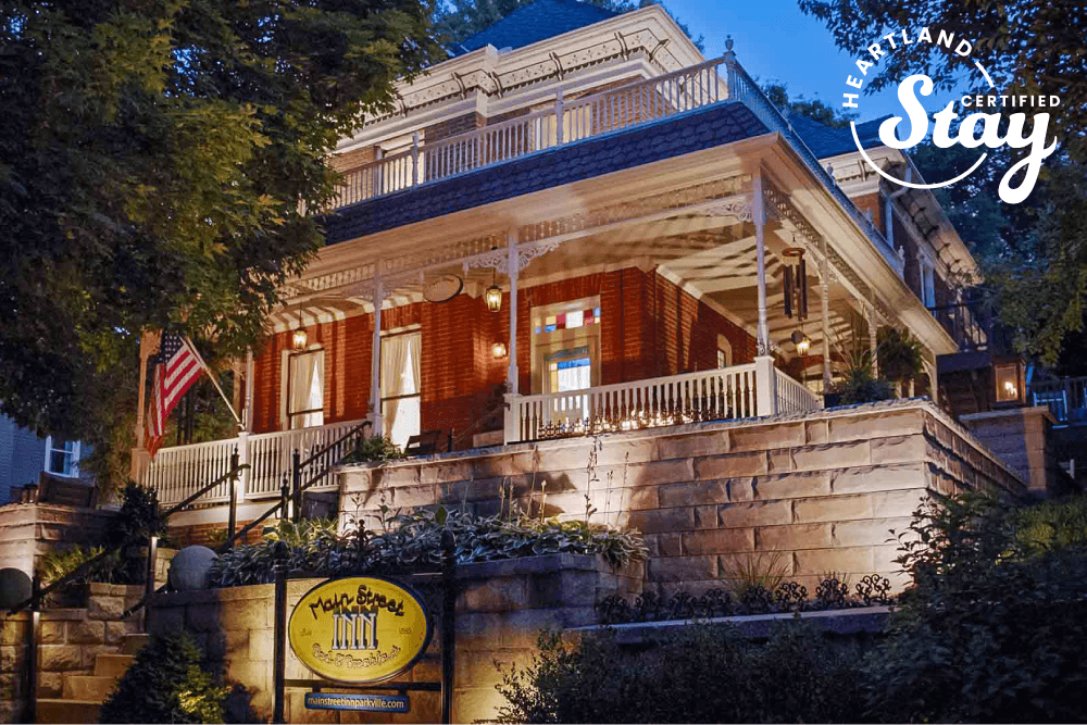 A charming, illuminated Victorian-style bed and breakfast with a welcoming front porch and American flag.