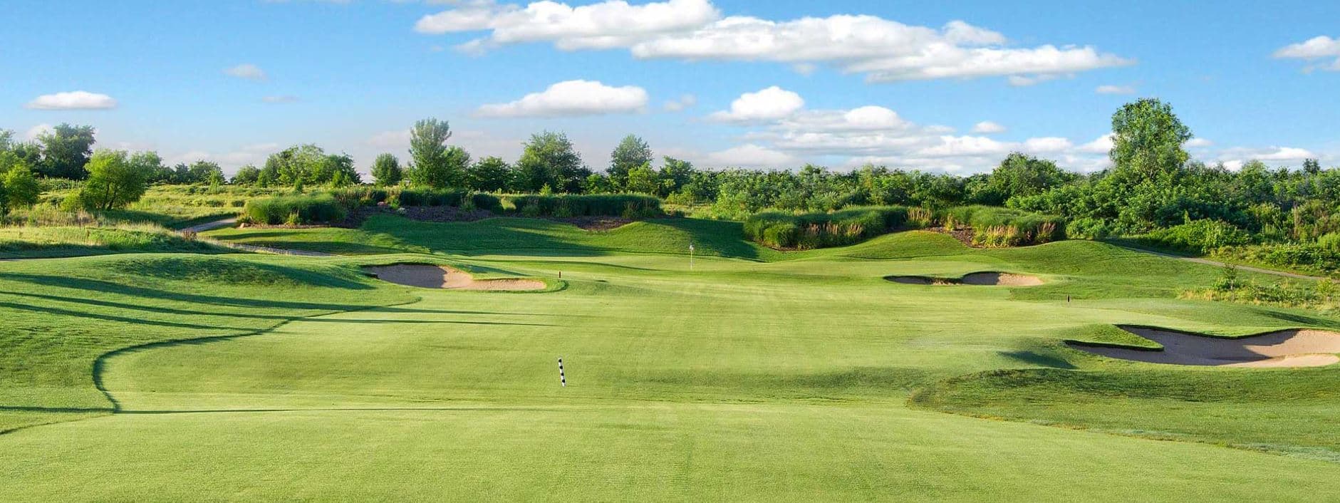 A lush green golf course landscape under a blue sky with fluffy clouds.