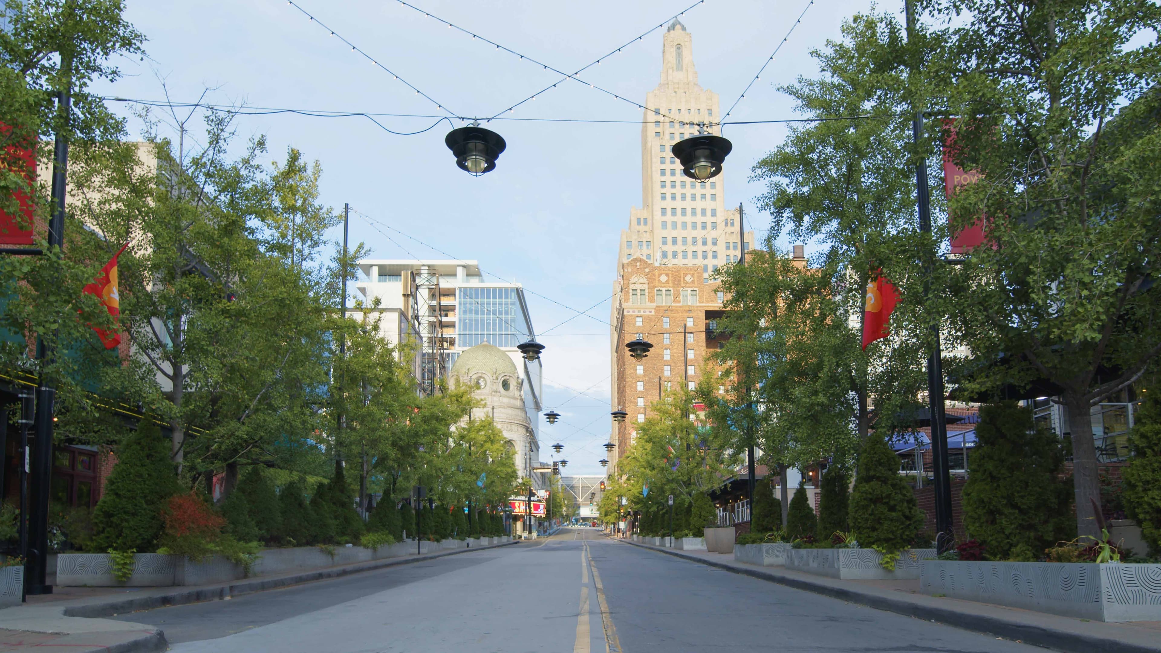 A deserted street lined with trees and buildings under a blue sky.