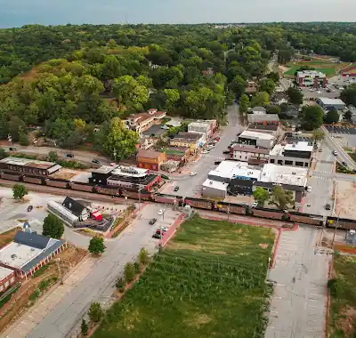 Aerial view of a small town with a mix of shops, greenery, and a train passing through.