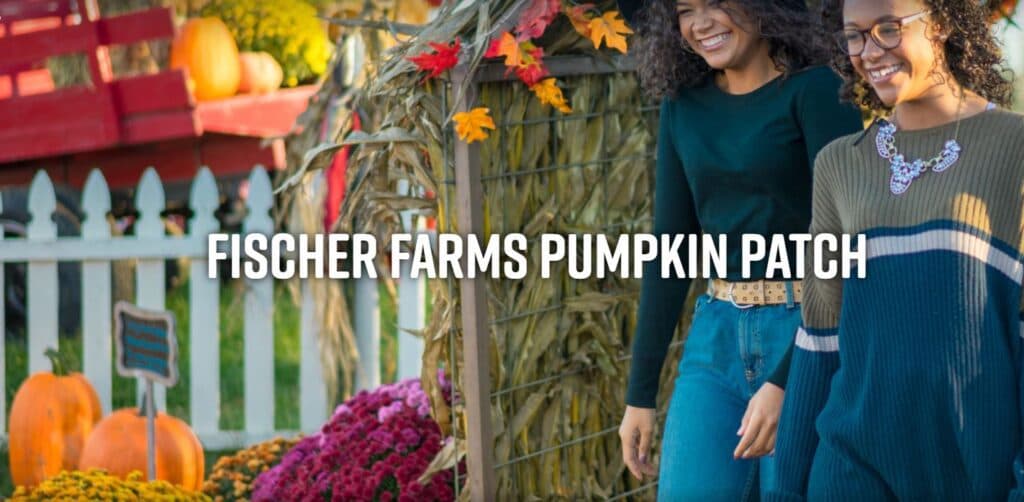 Two women walking through Fischer Farms Pumpkin Patch surrounded by pumpkins and colorful flowers.