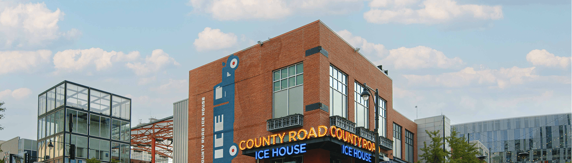 A modern brick building features large glass windows and a brightly lit sign for "County Road Ice House."