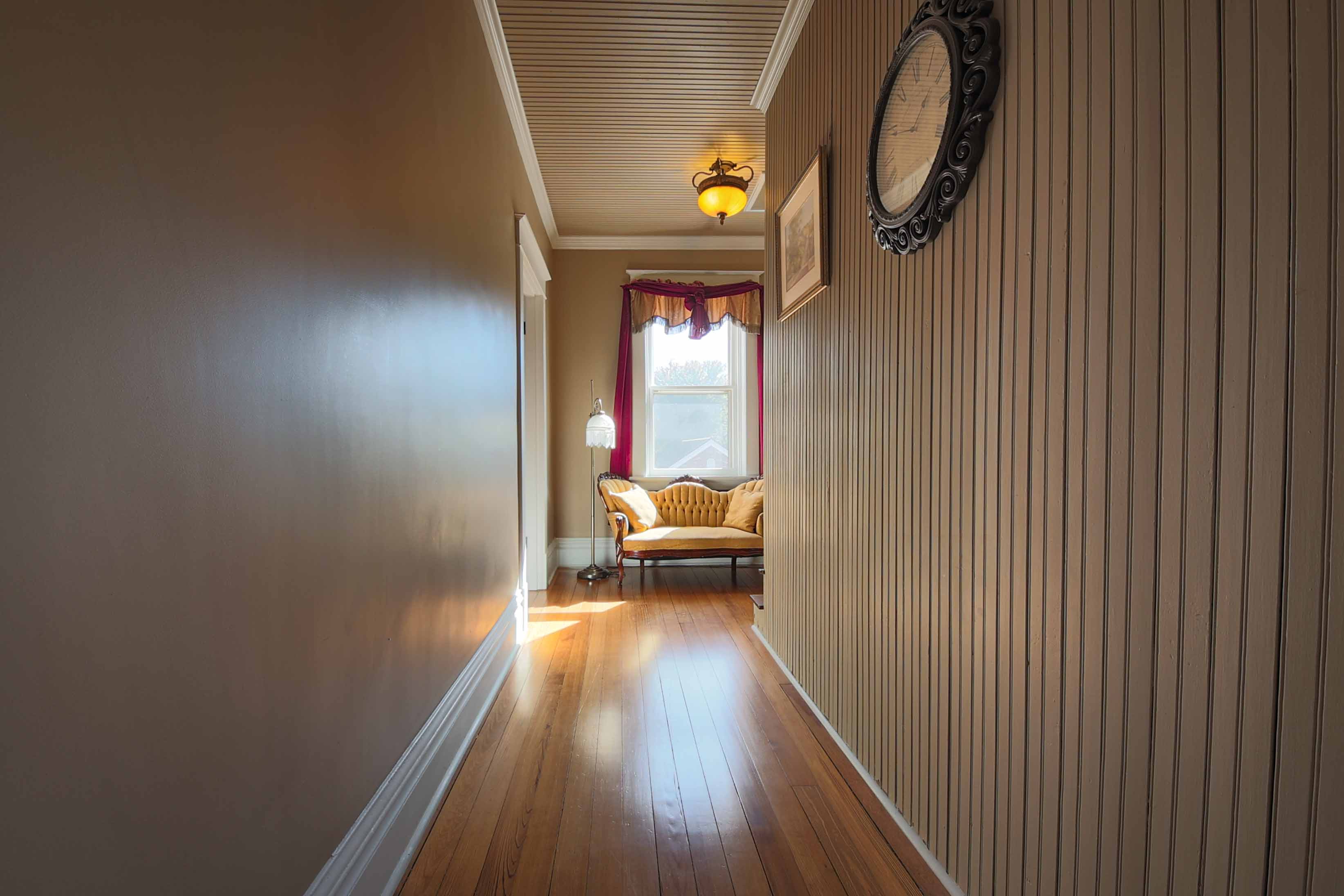 A sunlit hallway features a vintage couch by a window, with wooden flooring and decorative wall elements.