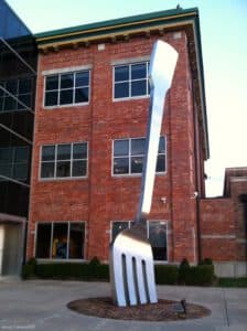 A large metallic fork sculpture stands in front of a brick building.